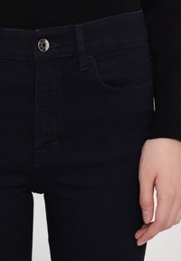 Mörkblå jeans med en slät textur, med ett framknäppe, femfickorsdesign och subtila sömsdetaljer.