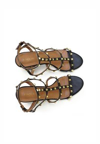 Zwarte bandjes sandalen met gouden piramide studs, leren materiaal, platte zool, verstelbare enkelriemen en bruine voetbeddetails.