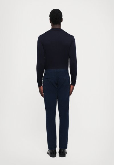Navy long-sleeve top paired with dark blue trousers. The outfit features a fitted design, smooth texture, and minimalistic styling.