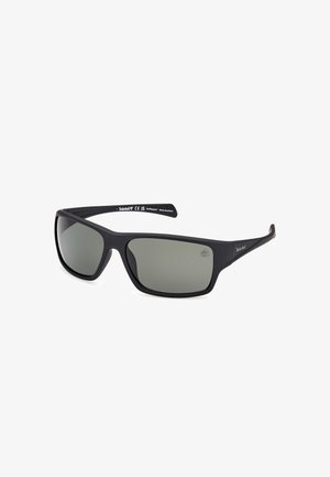 Gafas de sol Timberland con marco de acabado mate negro, lentes ahumados grises, forma curvada y logo en la patilla. Diseño duradero y ligero.