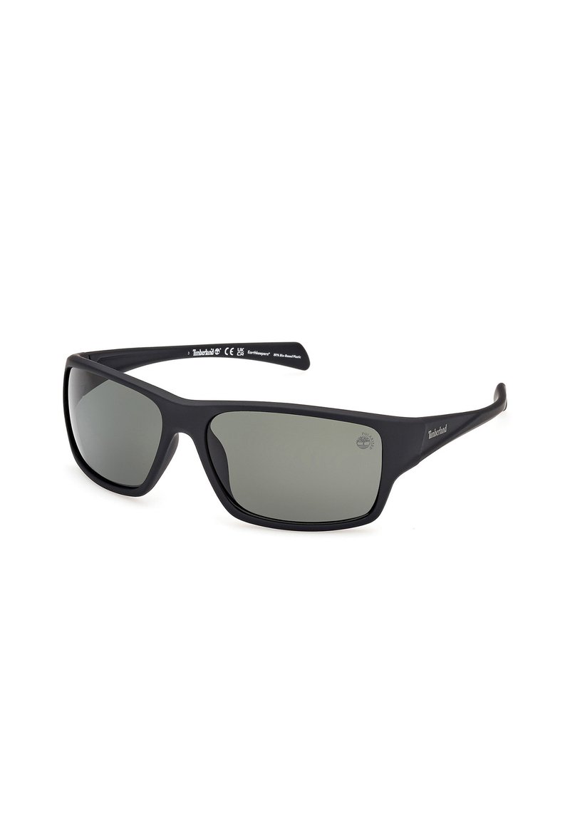 Gafas de sol Timberland con marco de acabado mate negro, lentes ahumados grises, forma curvada y logo en la patilla. Diseño duradero y ligero.