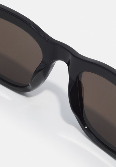 Occhiali da sole neri con montatura in plastica liscia. Lenti color marrone, forma leggermente curvata e senza hardware o loghi visibili.