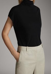 Haut noir à col montant en tissu lisse avec des manches courtes, associé à un pantalon beige clair ajusté avec des poches latérales.