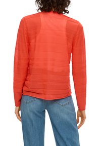 Chemise rouge à manches longues avec des rayures horizontales, texture transparente, encolure ronde et coupe décontractée, associée à un jean bleu clair.