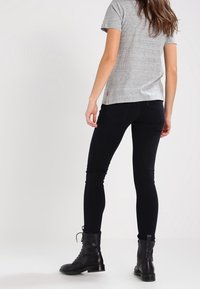 T-shirt gris à manches courtes associé à un jean skinny foncé et des bottes noires à lacets ; tissu lisse et coupe ajustée.