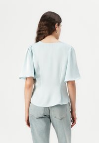 Blusa celeste con maniche corte a sbuffo. Tessuto morbido con scollatura rotonda e orlo leggermente svasato. Indossata con jeans in denim chiaro.