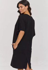 Czarna sukienka z krótkim rękawem, o luźnym kroju, z bocznymi kieszeniami i rozcięciem z tyłu dla swobody ruchów. Gładki materiał i prosty fason.