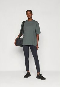 Μπλουζάκι σε χαλαρή εφαρμογή σε σκούρο γκρι χρώμα, συνδυασμένο με μαύρο κολάν και μαύρα αθλητικά παπούτσια. Τσάντα ώμου με απλό σχέδιο.