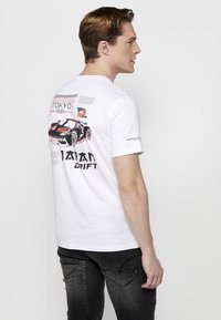 Baltas medvilnės marškinėlis su automobilio grafika, tekstu "TOKYO" ir "DRIFT", raudonais ir juodais akcentais ant nugaros. Laisvas pjūvis.