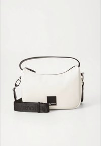 Hvit rektangulær skulderveske med svart justerbar stropp og liten svart merkeetikett foran, mot en ensfarget lys bakgrunn.