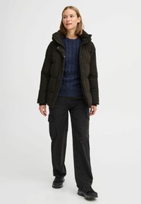 Jachetă puffer neagră cu glugă, combinată cu un pulover navy cu model de tricot, pantaloni cargo negri și adidași negri. Design simplu, funcțional.