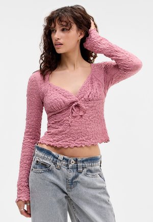 Ribbed, long-sleeve, cropped top in dusty pink with a v-neck and drawstring detail at the front. Soft, textured fabric with scalloped hem.