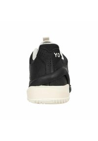 Schwarzer Sneaker mit einem glatten Lederobermaterial, kontrastierenden weißen Akzenten, einem gepolsterten Fersenbereich und sichtbarem Branding auf der Rückseite.