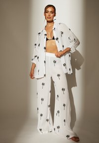 Camisa blanca de manga larga ligera y pantalones de pierna ancha con patrón de palmeras negras; bikini negro; tela suave y texturizada.