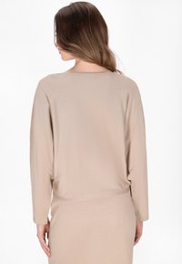 Beige dlouhý rukáv s uvolněným střihem. Měkká, strukturovaná tkanina s kulatým výstřihem a mírně zkráceným lemem.