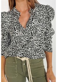Blouse à motifs noir et blanc avec un col en V, des manches bouffantes et des détails froncés ; associée à un pantalon vert olive avec des poches avant.