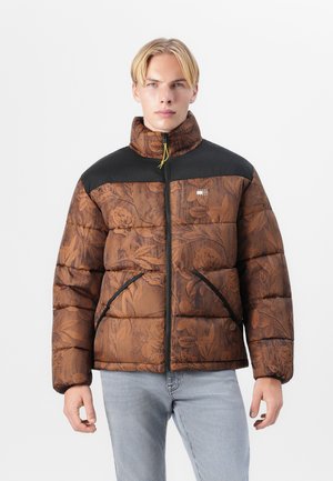Bruine pufferjack met bloemenpatroon, zwarte schouderaccenten, hoge kraag en ritssluiting. Beschikt over zijzakken en een soepele textuur.