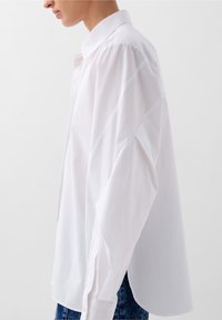 Camicia bianca a colletto con maniche lunghe, caratterizzata da una vestibilità comoda e una texture morbida, abbinata a jeans di denim blu.