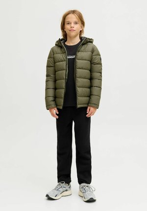 Zelená puffer bunda s prošívaným designem a kapucí, nošená přes černé tričko, v kombinaci s černými tepláky a šedými teniskami.