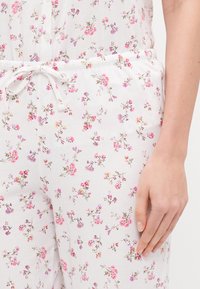 Ziedu pidžamu komplekts no mīksta balta auduma ar rozā un violetiem ziedu rakstiem. Elastīga jostasvieta ar auklu un pogu detaļu augšdaļā.