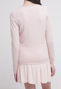 Top de manga larga de color rosa claro, fabricado con material suave y con un diseño ajustado. El detalle de la falda plisada añade textura, creando un look en capas.