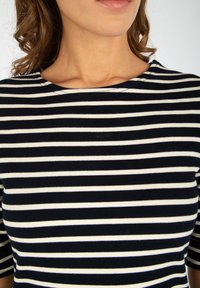 Top a righe bianche e nere con scollo a barca, realizzato in un tessuto liscio. Presenta maniche a tre quarti e una silhouette aderente.