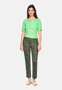 Green short-sleeve top paired with black pants featuring a green leaf pattern. The model wears light-colored flat shoes.