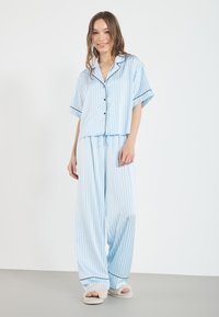 Light blue striped pajama set features short-sleeve top with black buttons and matching wide-leg pants. Soft fabric, casual design.
