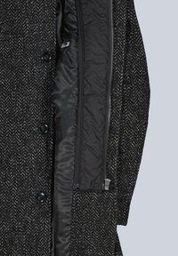 Schwarz-weiß gemusterter Herringbone-Mantel mit Reißverschluss an der Innenseite, schwarzer Futter- und Knopfverzierung; Außenmaterial aus strukturiertem Wollstoff.