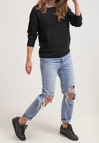 Černý pletený svetr, světle modré džíny s roztrhanými koleny a černé tenisky s červenými detaily. Ležérní styl outfitu.