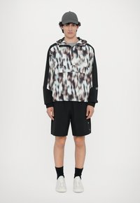 Hanorac cu glugă din material de tip pull-over, cu un model abstract în nuanțe de albastru, negru și piersică; mâneci negre; asortat cu pantaloni scurți negri; adidași albi.