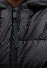 Doudoune noire avec col montant, fermeture éclair et design matelassé. Le matériau semble lisse avec un léger éclat.