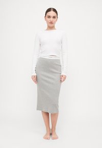 Balta ilga rankovė crop viršūnė, derinama su pilku pieštukiniu sijonu, pasižyminčiu prigludusia forma ir lygiu paviršiumi, su Calvin Klein juosta.