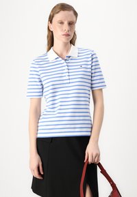Stripet polo-skjorte med blå og hvite striper og hvit krage, laget av bomull, kombinert med et svart skjørt og en rød veske.