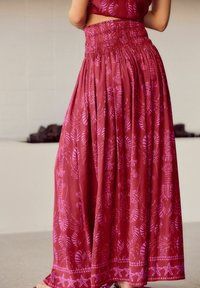 Maxi nederdel i bordeaux stof med pink blad- og søstjernemønstre, der har en smocked talje og et flydende, struktureret design.