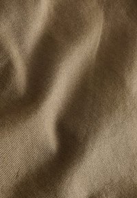 Tan stof met een gladde, matte textuur, gekenmerkt door subtiele rimpelingen en een fijne ribstructuur, wat diepte en variatie in kleur creëert.