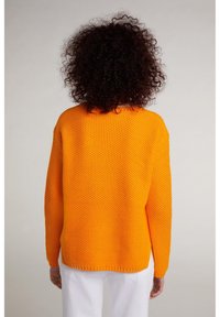 Maglione arancione lavorato a maglia con un design testurizzato a trama aperta, caratterizzato da maniche lunghe e una vestibilità morbida, visto da dietro su uno sfondo neutro.