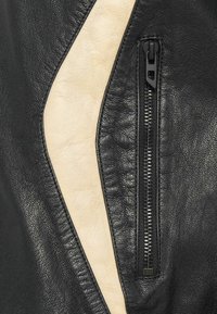 Μαύρο δερμάτινο μπουφάν με κρεμ πάνελ, ασύμμετρο σχέδιο και εμφανές φερμουάρ. Υφή με ανάγλυφη επιφάνεια και λείες λεπτομέρειες.