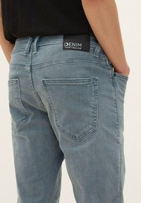 Jean en denim bleu clair avec une coupe droite, comportant deux poches arrière et un patch noir de marque au niveau de la taille.