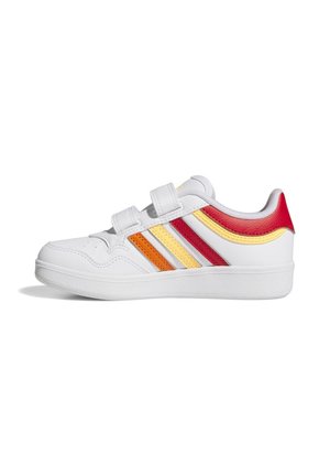 Zapatilla deportiva blanca con franjas en naranja, amarillo y rojo, dos cierres de velcro y suela texturizada, mostrada desde el lado exterior.