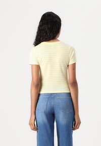 Top à manches courtes rayé jaune et blanc avec un col rond, associé à un jean en denim bleu taille haute.
