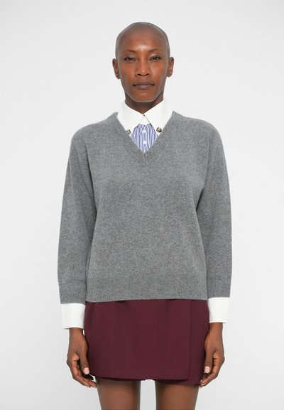Gray knitted v-neck sweater worn over a white collared shirt with blue stripes. The model also wears a maroon skirt. Smooth texture.