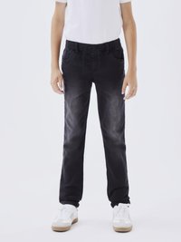 Jeans en denim noir avec une finition délavée, deux poches avant, une taille élastique et un cordon de serrage ; stylés avec des baskets blanches.