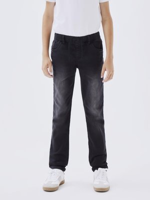 Jeans de mezclilla negra con un acabado desgastado, dos bolsillos frontales, cintura elástica y cordón; combinados con zapatillas blancas.