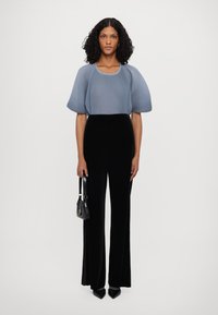 Haut à manches courtes côtelé bleu clair associé à un pantalon en velours noir taille haute et à jambes larges ; le mannequin tient un petit sac à main noir.