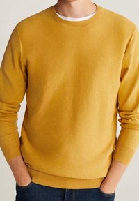 Hořčicově žlutý svetr s kulatým výstřihem, strukturovaným pleteným vzorem a žebrovanými manžetami a lemem. Nošený přes bílou spodní košili.