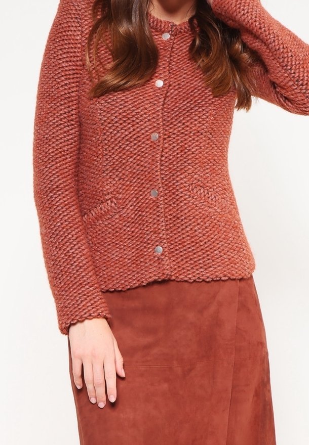Femme portant un cardigan en maille texturée couleur rouille avec des boutons argentés et une jupe en suède assortie couleur rouille.
