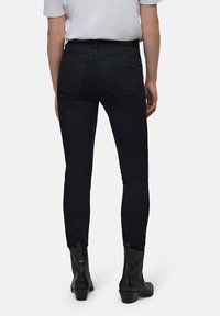 Jeans skinny de denim negro con cintura alta, que cuentan con dos bolsillos traseros y una textura suave. Combinados con botines negros.