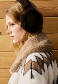 Fake pels ørevarmere i mørkebrun, blød krave i beige og et mønstret creme- og brunt yderstof med zigzag-accenter. Træbaggrund.