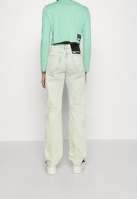 Mint green cropped long-sleeve top, paired with light green denim jeans featuring a relaxed fit, patch pockets, and contrasting tags on the waist.
